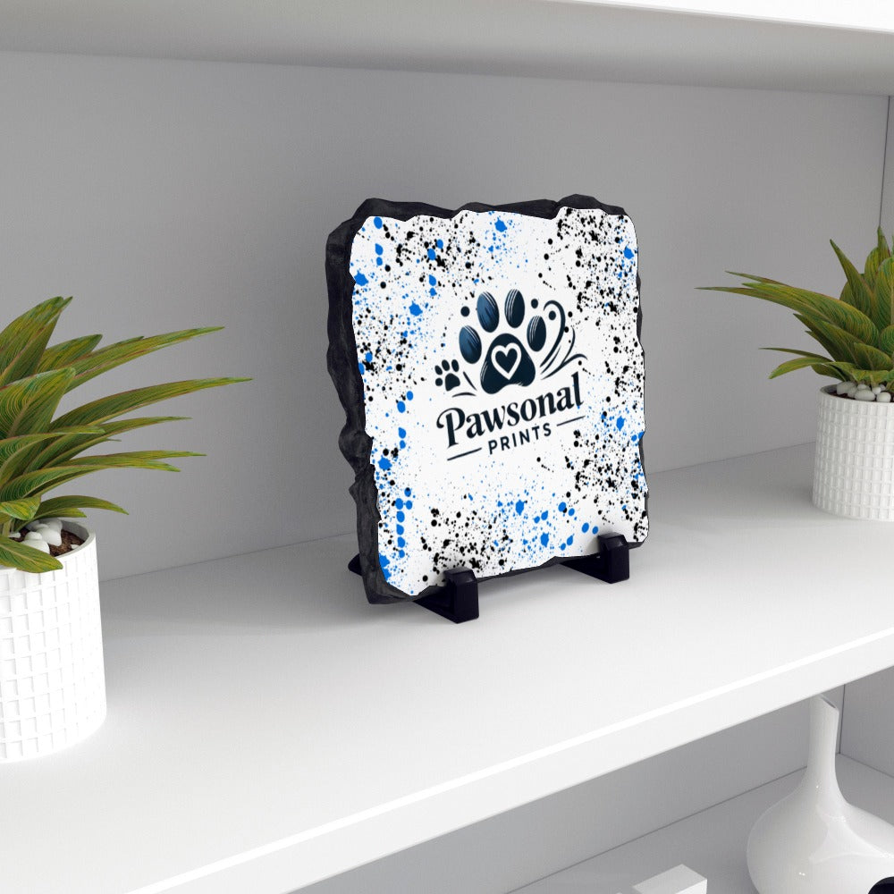 A rectangular personalised photo rock slate on a white shelf in a living room featuring a high-resolution printed image, mounted on a natural stone surface with rugged, chiseled edges. The slate is displayed on a black plastic stand, ideal for home or office déco